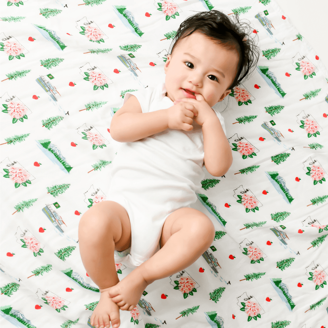 White muslin swaddle blanket with a colorful map of Washington State, featuring landmarks and playful illustrations.